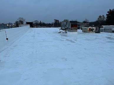 Flat, white commercial roof with HVAC units, under a cloudy sky.