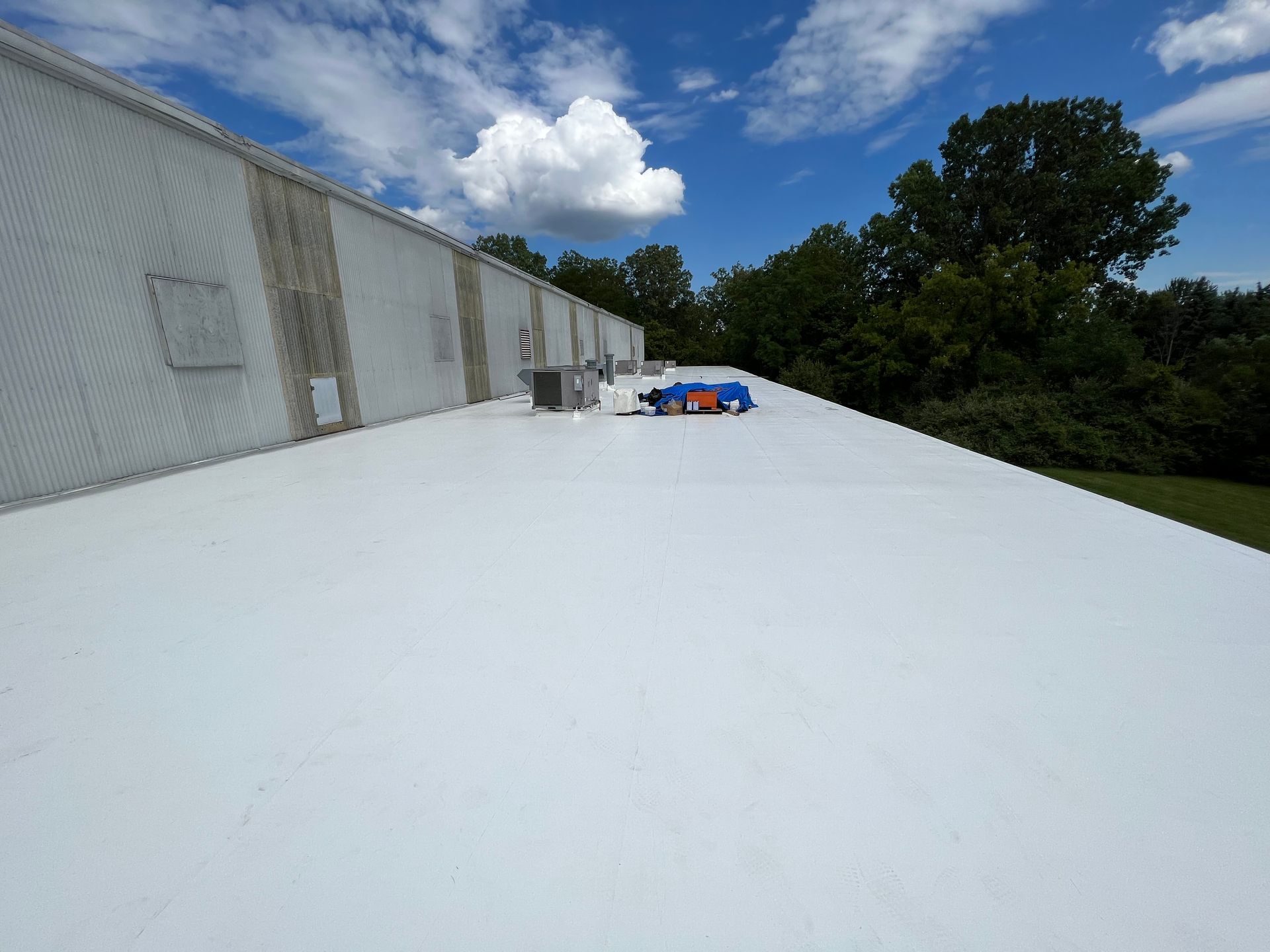 White commercial roof with a cloudy sky and green trees in the background.