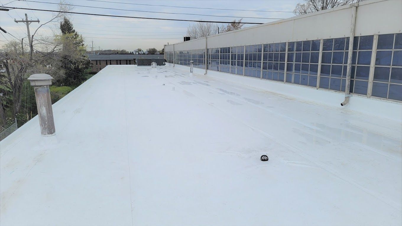 A flat, white roof with a small black object on it, next to a building with glass windows.