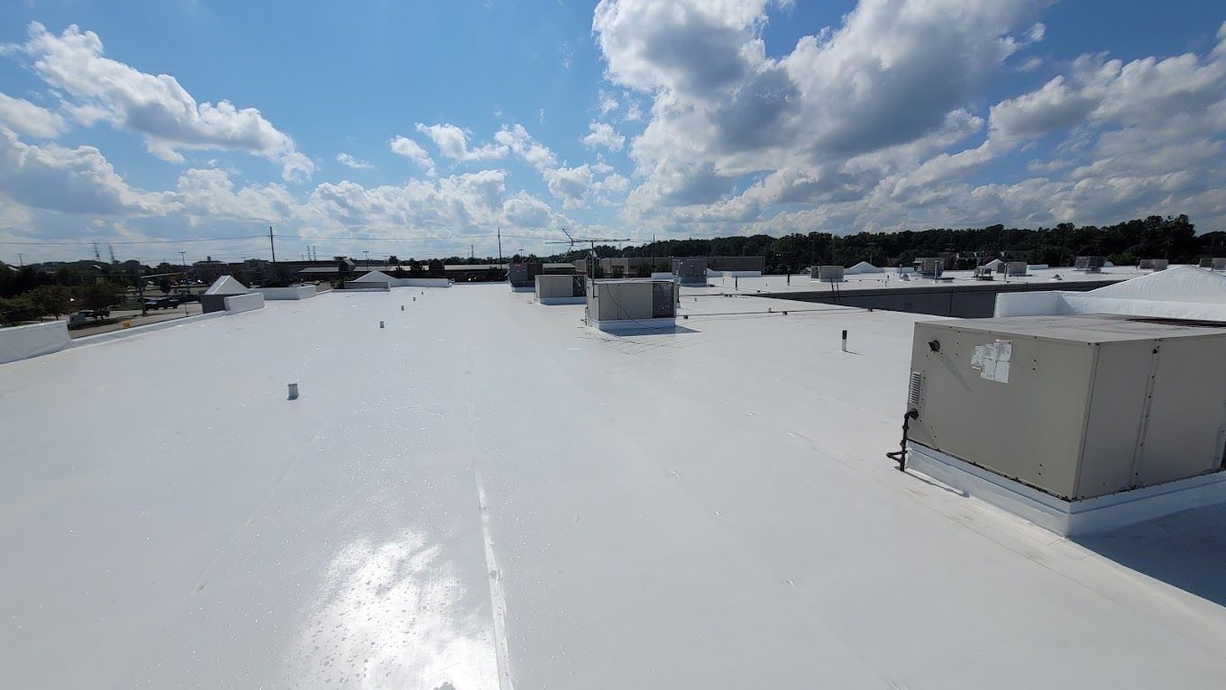 White roof of a building under a bright blue sky with fluffy clouds; air conditioning units are visible.