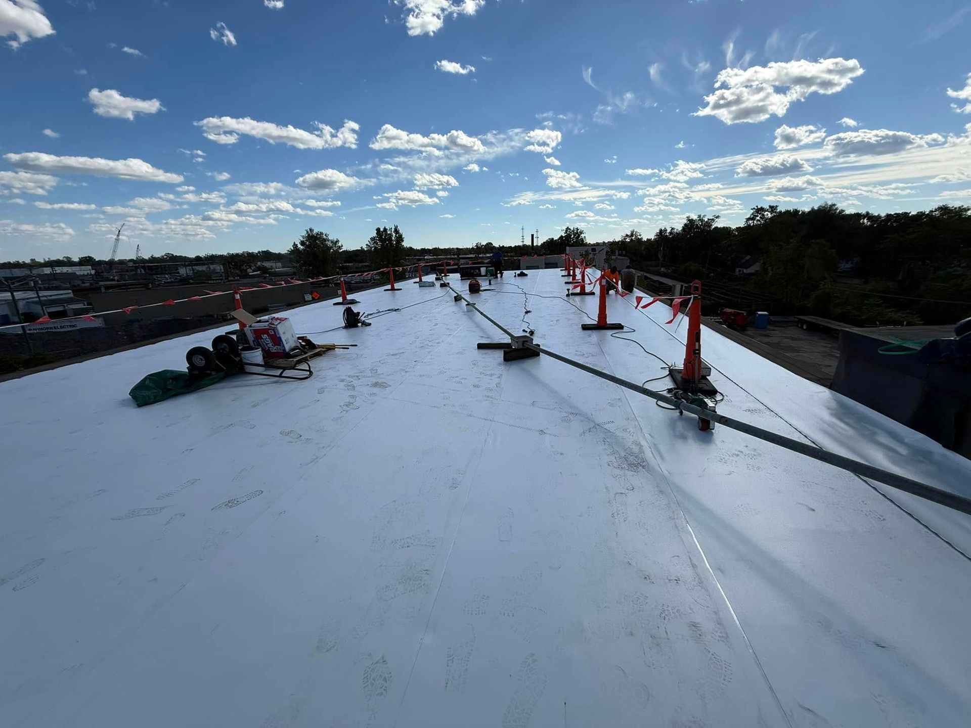 Workers on a reflective roof install safety equipment under a partly cloudy sky.
