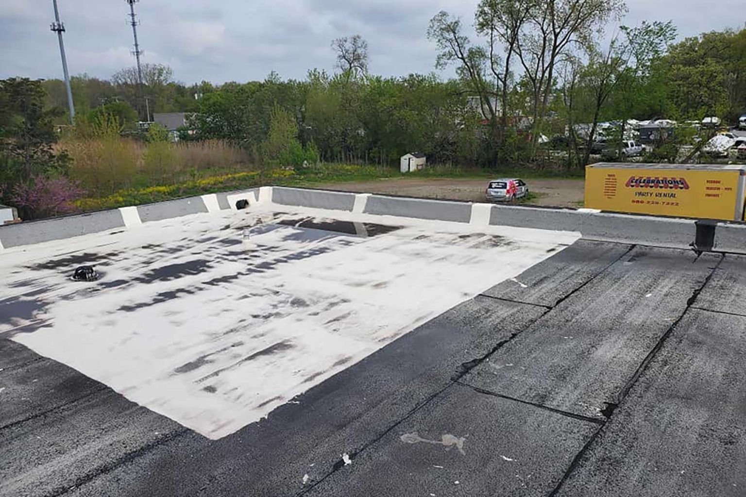 Flat roof with black asphalt and white reflective coating. Yellow sign in background.