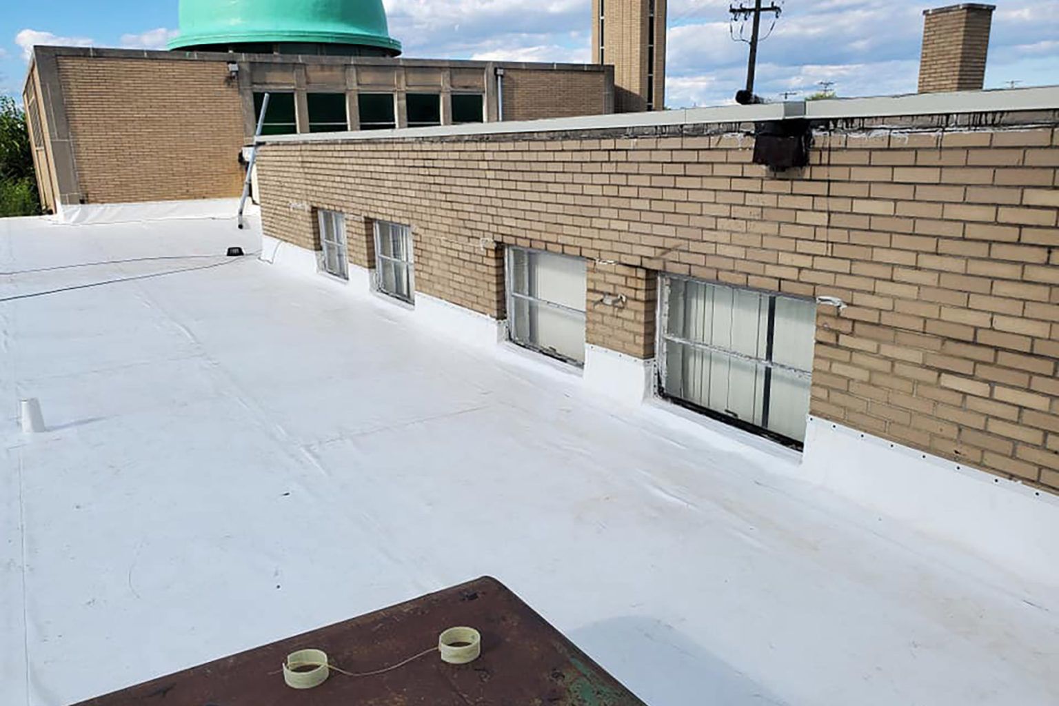 White flat roof next to a brick wall with windows. A green domed building is in the background.