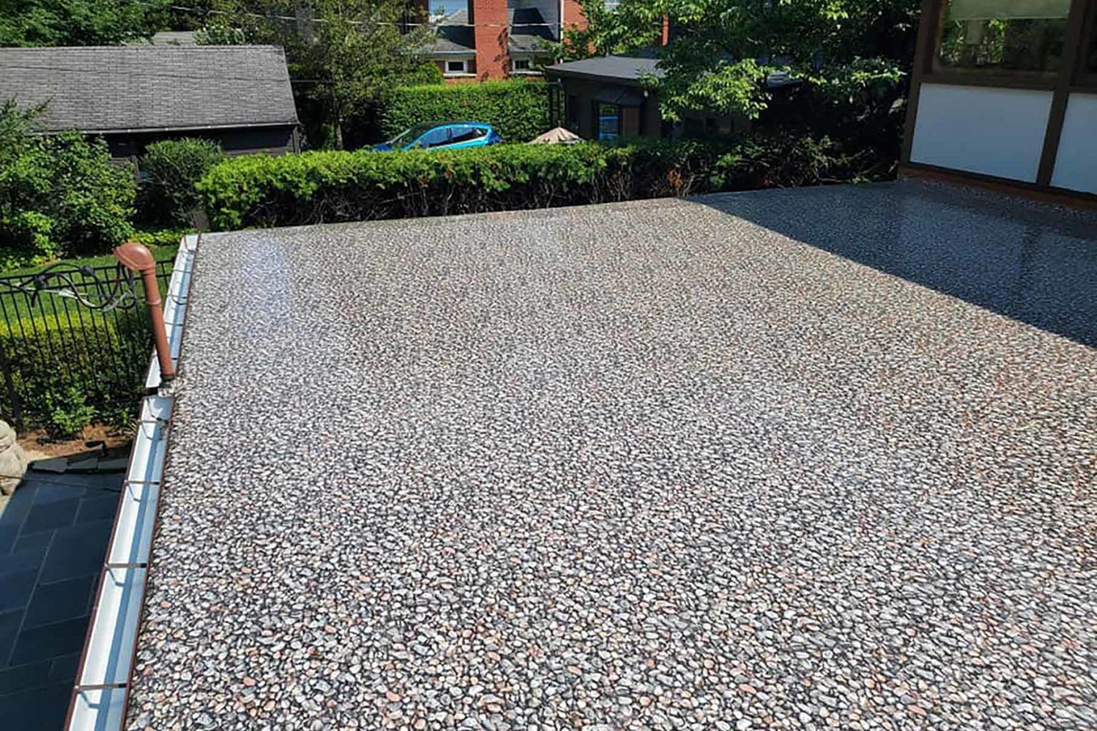 Gravel-covered rooftop with a gutter on the left. Lush green hedges and trees in the background.