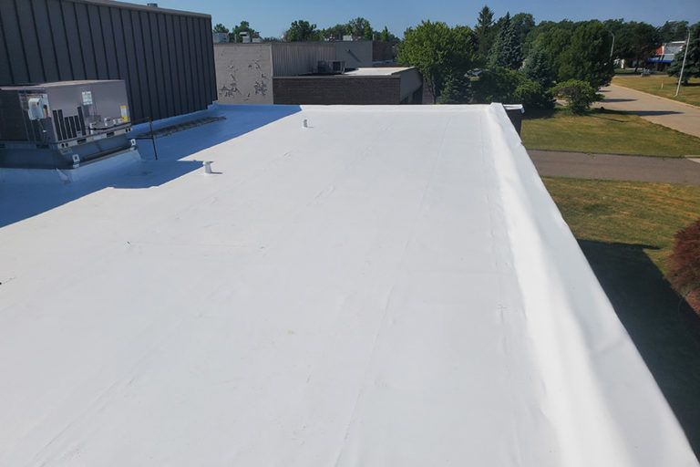 White flat roof with an air conditioning unit on a commercial building, with trees and grass nearby.