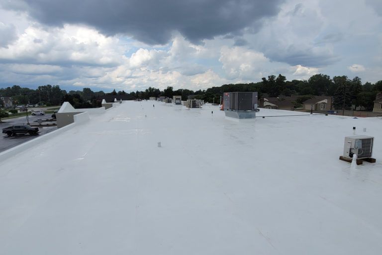 White commercial roof with air conditioning units, cloudy sky.