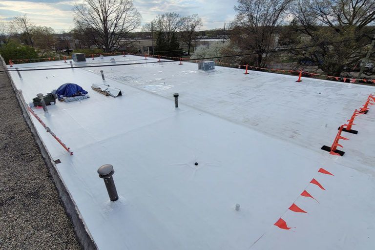 Workers on a flat roof installing white reflective material, with orange safety markers and a blue tarp.