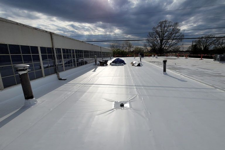 White commercial rooftop with vents, a small tent, and cloudy sky.