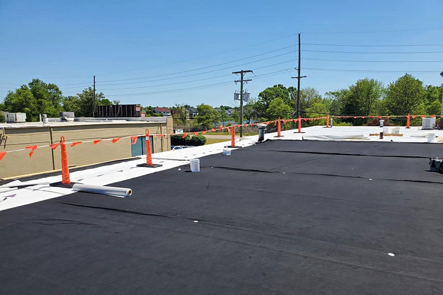 Black tar roofing with orange safety barriers under a blue sky.