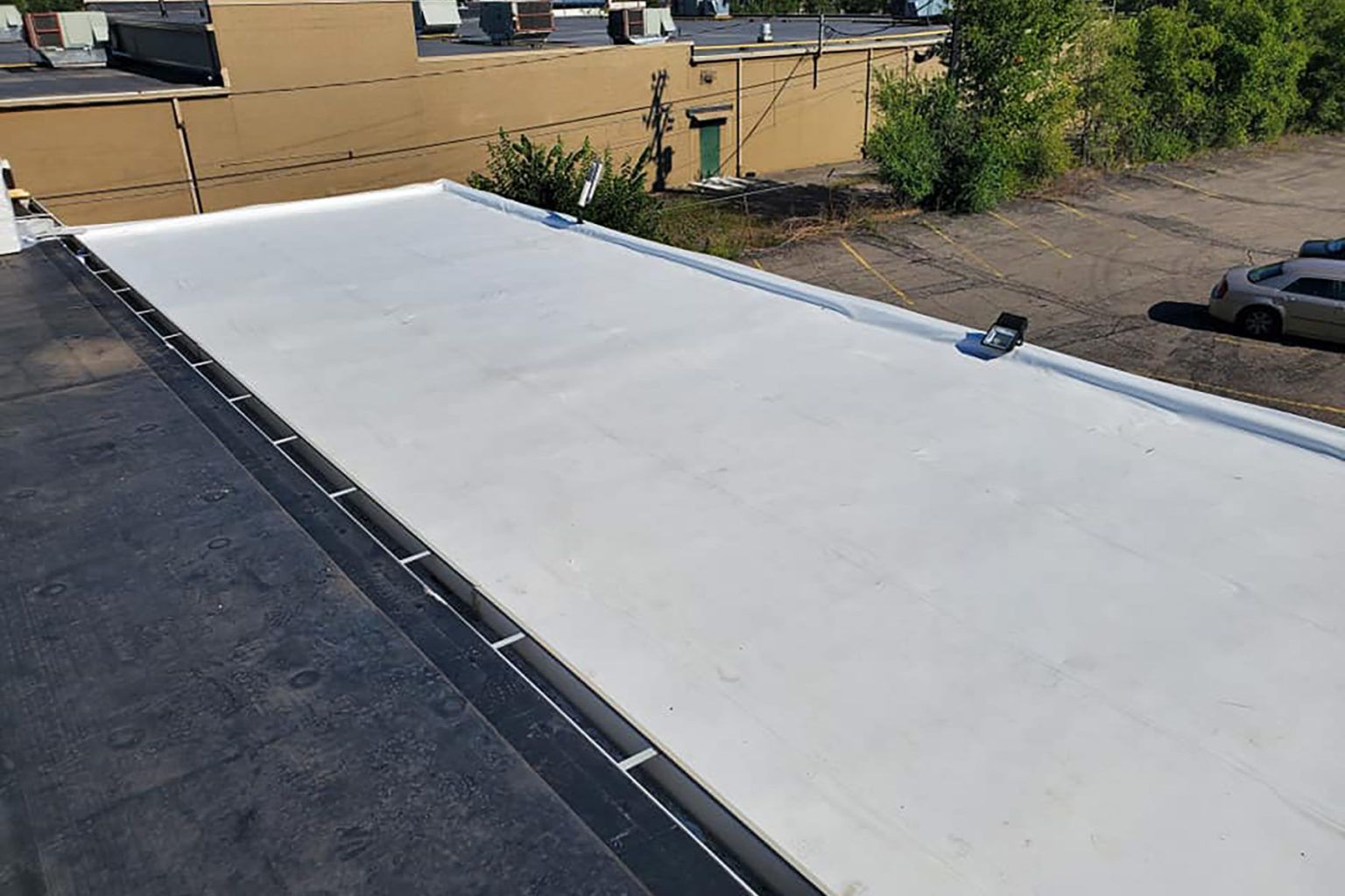 A flat white commercial roof with dark trim, overlooking a parking area and other buildings.