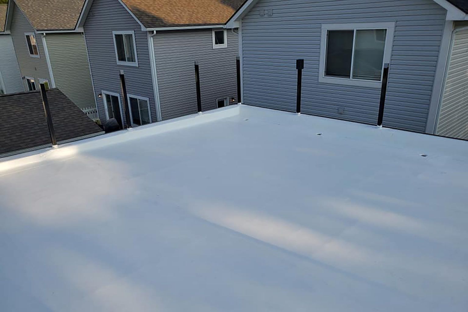 A flat, white roof with black pipes, viewed from above with houses in the background.