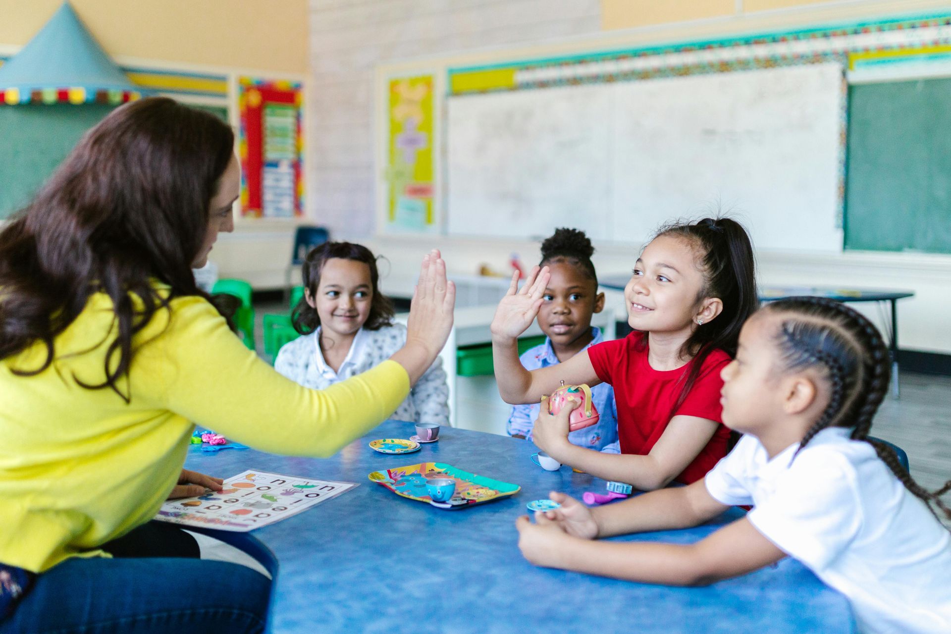 A teacher is giving a high five to a group of children in a classroom.