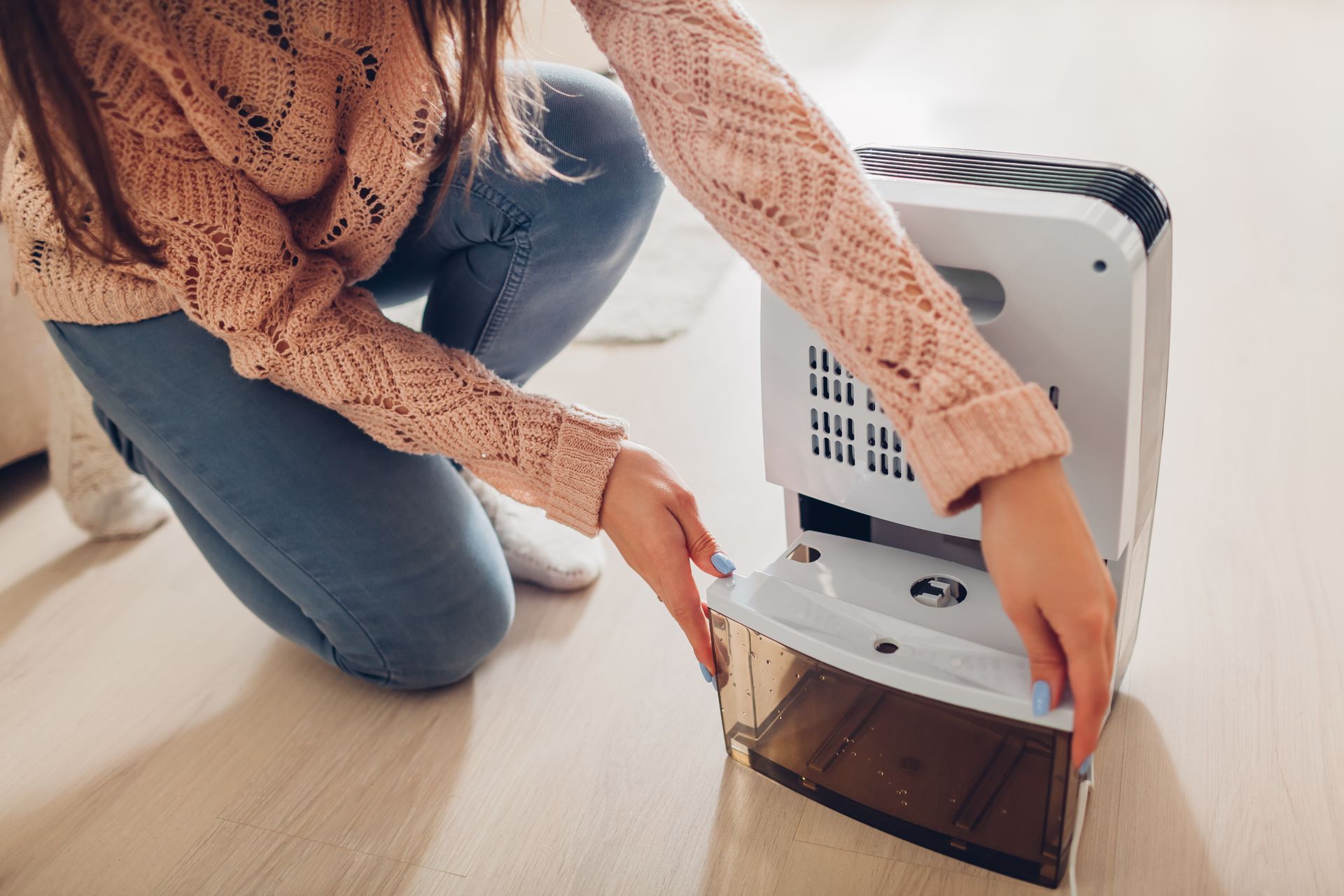 Person kneeling beside a white pet carrier, opening the door on a light wood floor.