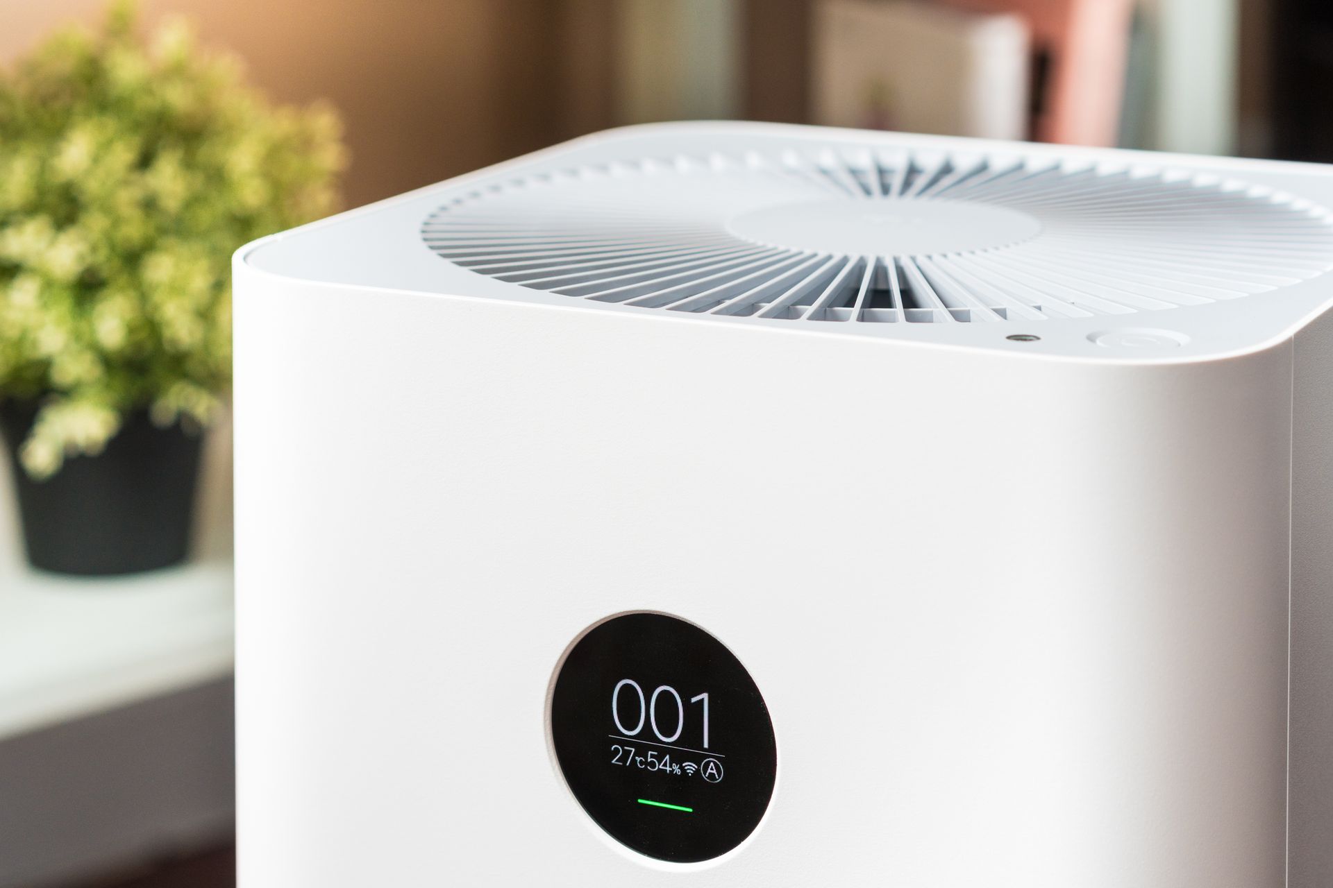 White air purifier with circular display on a windowsill, showing “001” in a bright room.