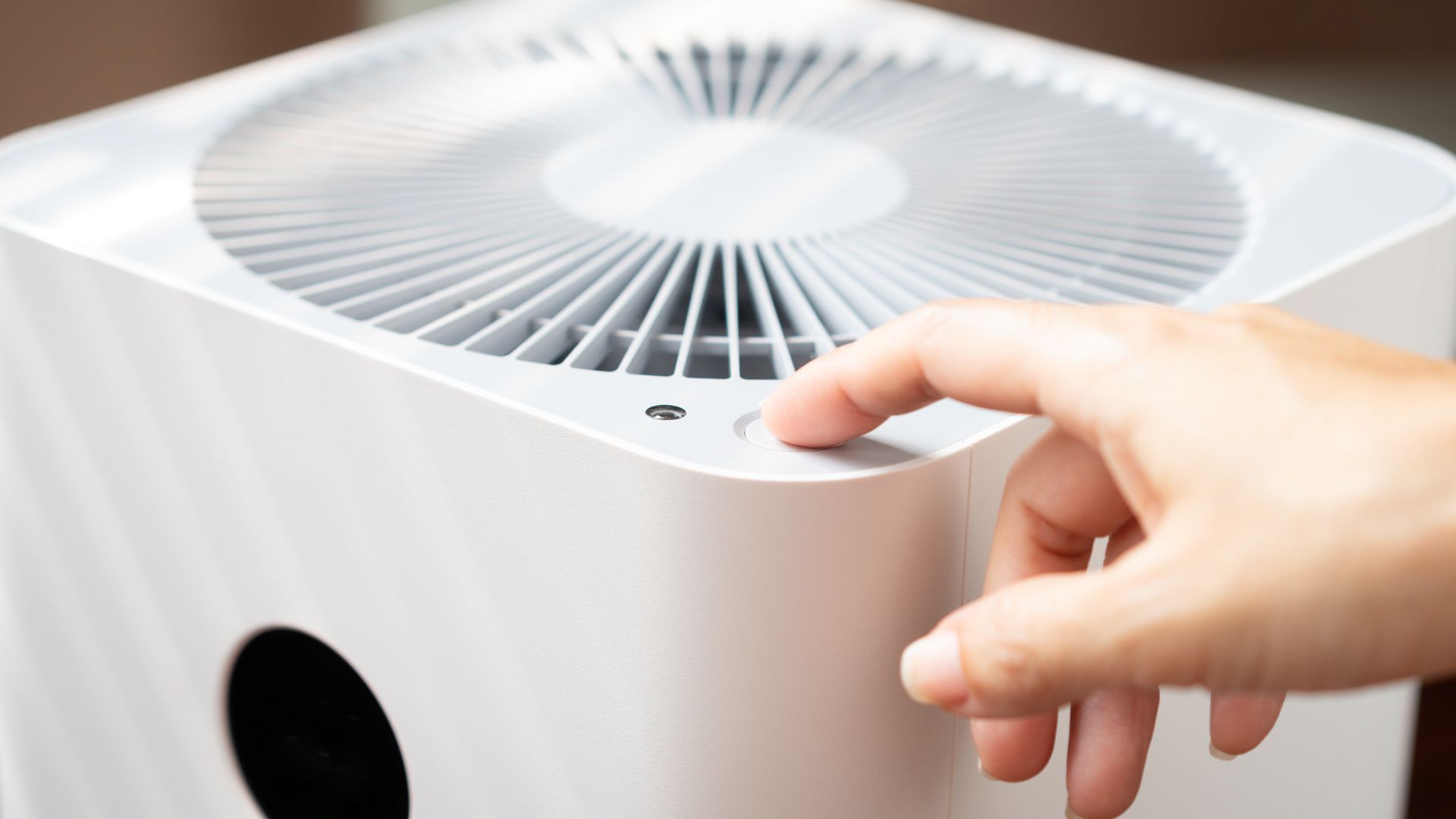 Hand pressing a white air purifier’s top control panel