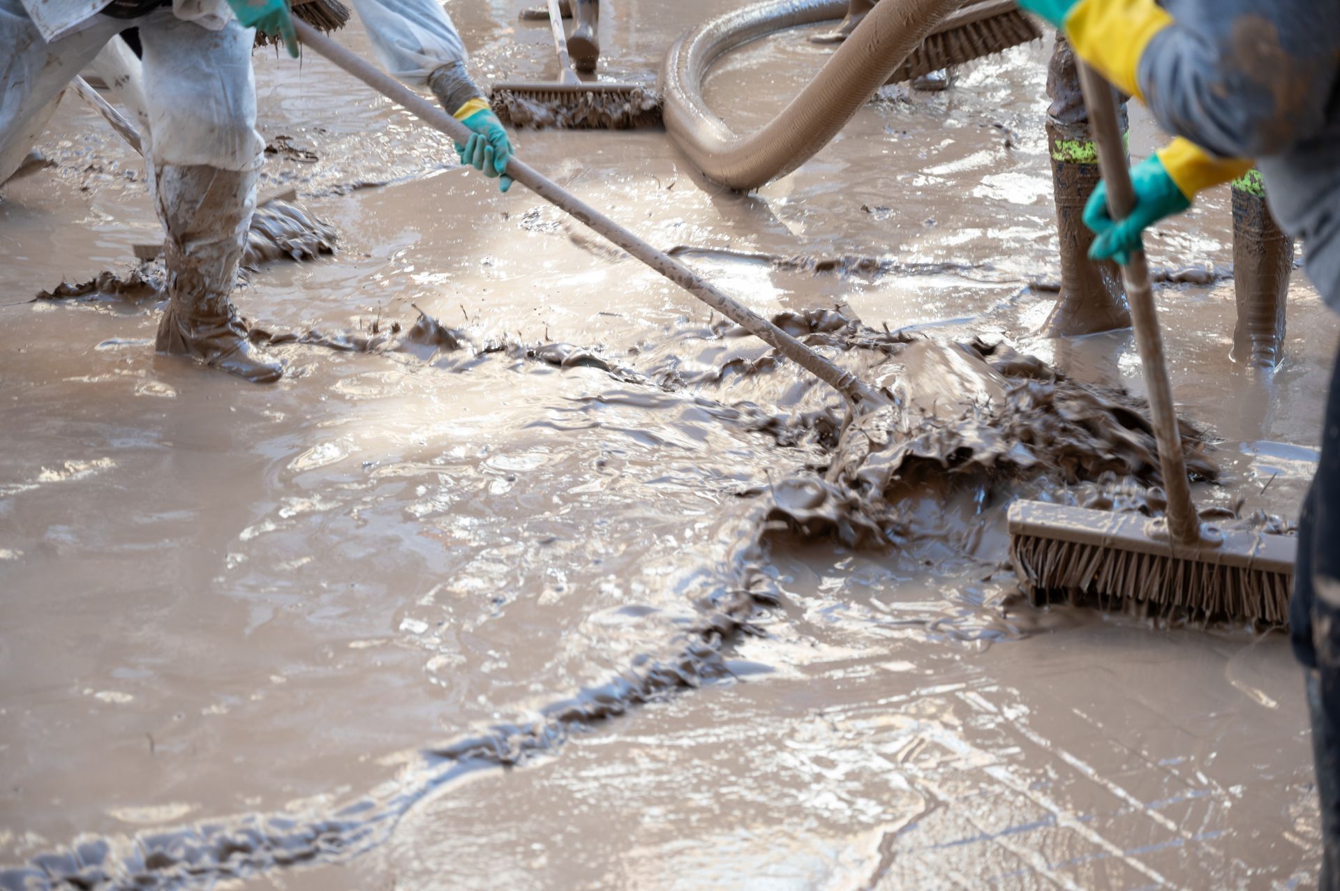 Workers cleaning muddy floodwater with brooms and hoses on a wet street