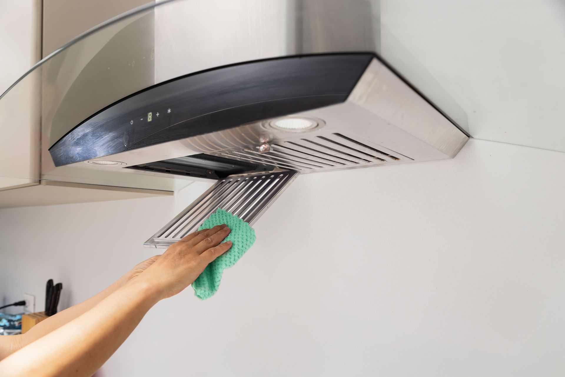 Hand wiping grease from a kitchen range hood with a green cloth