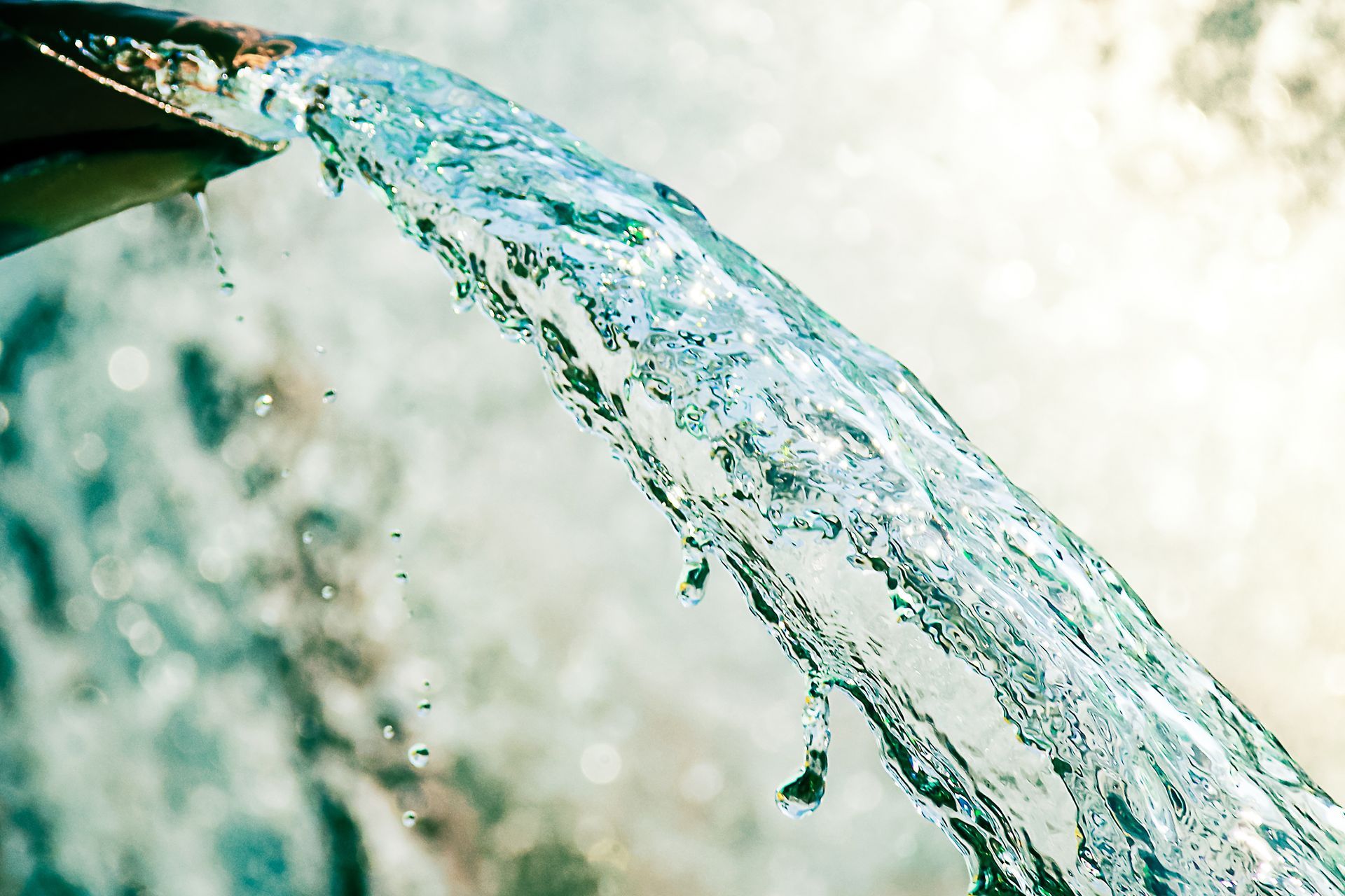 Clear water pouring from a spout with splashing droplets against a bright background