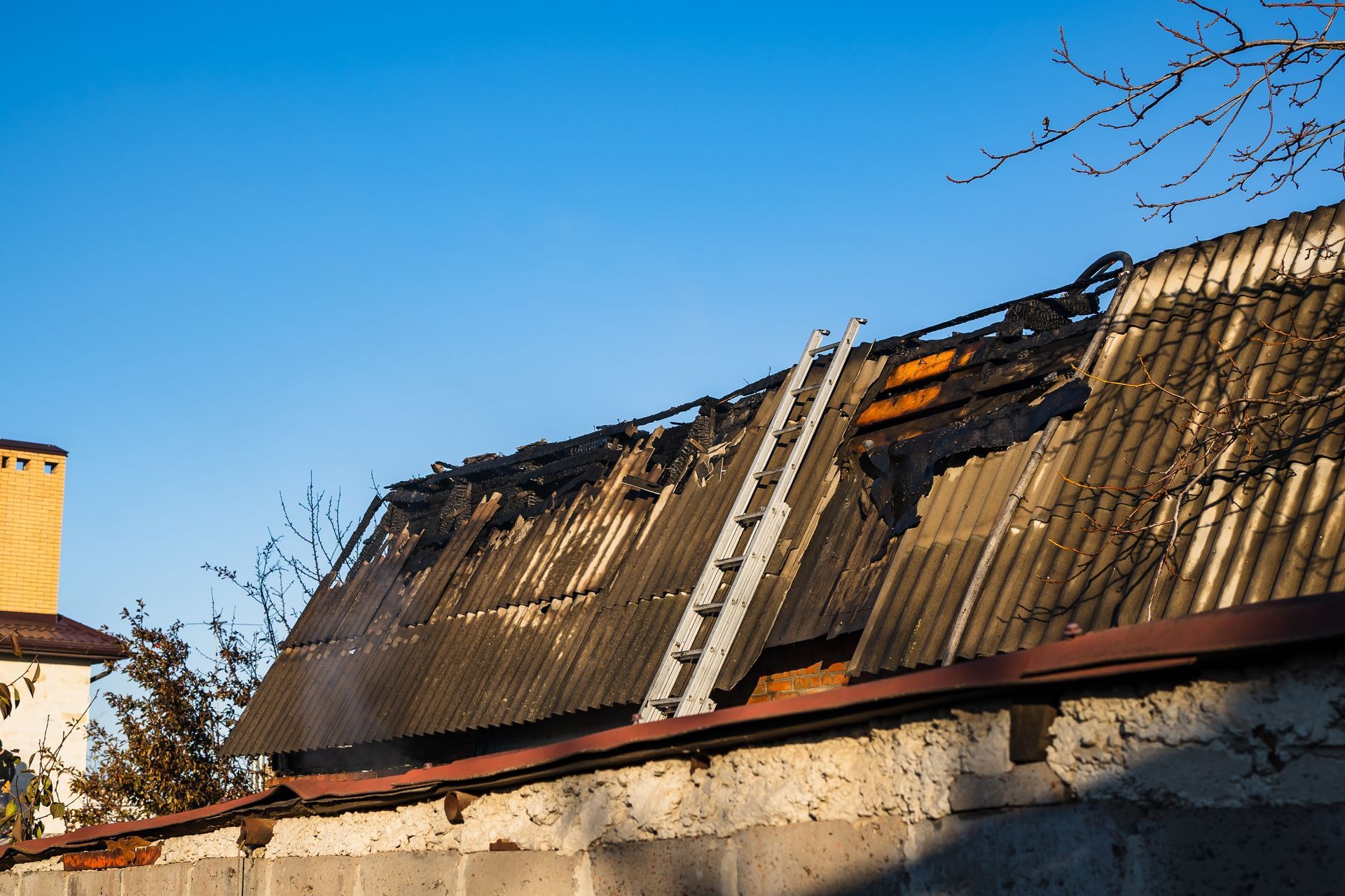Burned roof with charred wooden shingles and smoke damage under a clear blue sky
