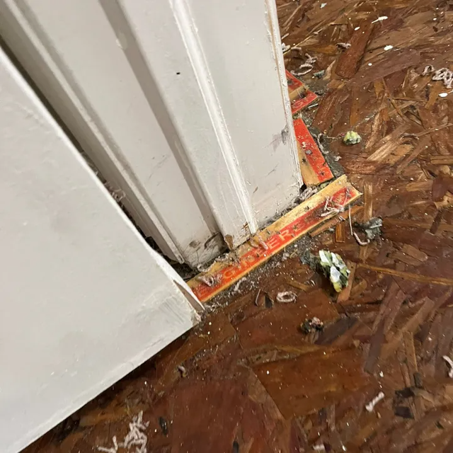 Close-up of a white door frame edge with chipped orange trim on a brown patterned floor.