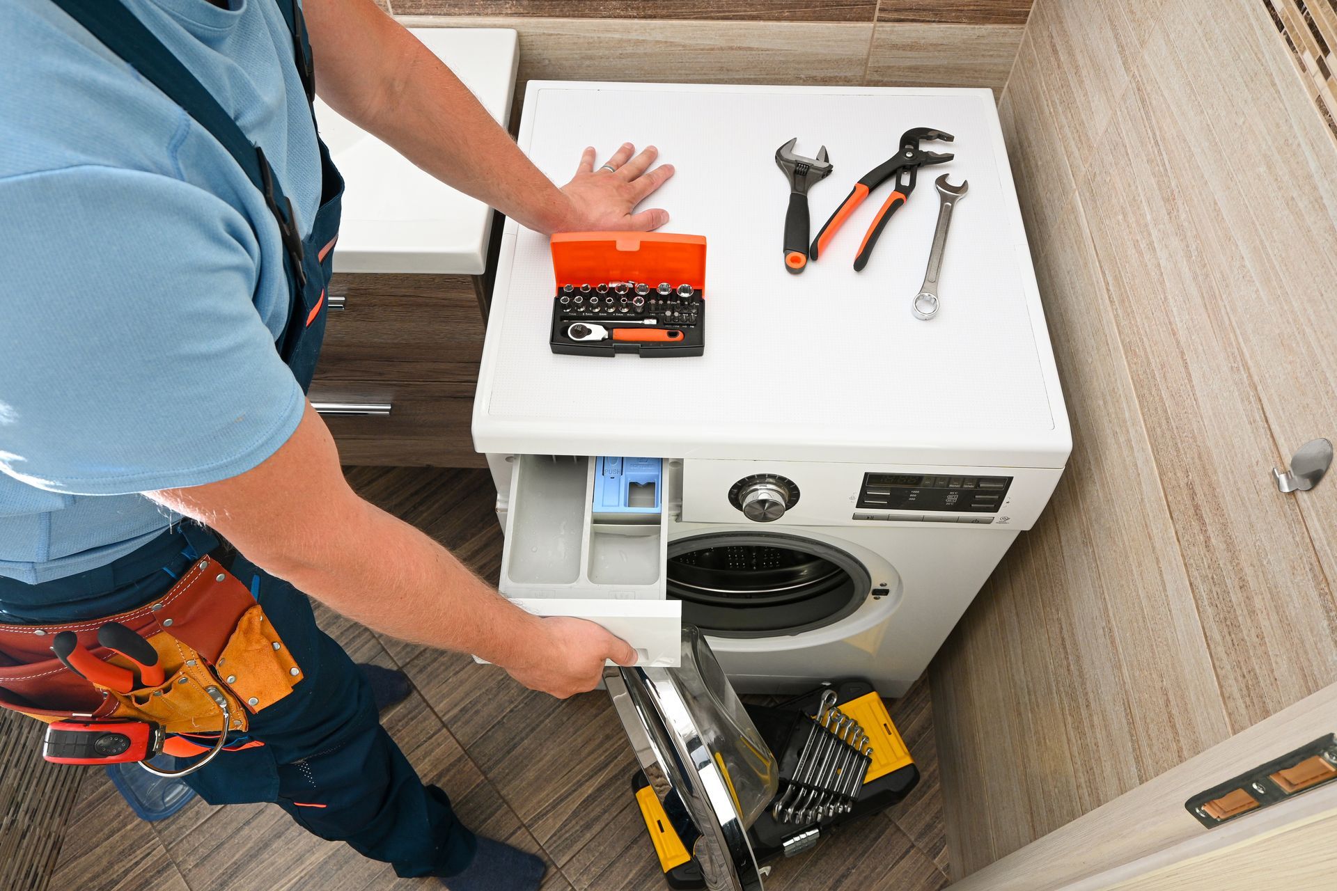Technician servicing a washing machine with tools on top in a laundry room.