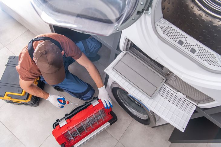 Technician cleaning a washing machine with a red vacuum and cloth, viewed from above. Technician cleaning a washing machine with a red vacuum and cloth, viewed from above.