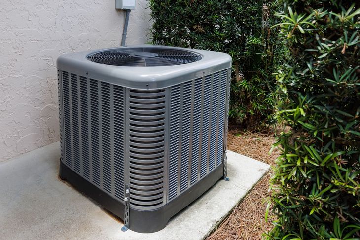 Outdoor air conditioner unit beside a house wall on a concrete pad near shrubs Outdoor air conditioner unit beside a house wall on a concrete pad near shrubs