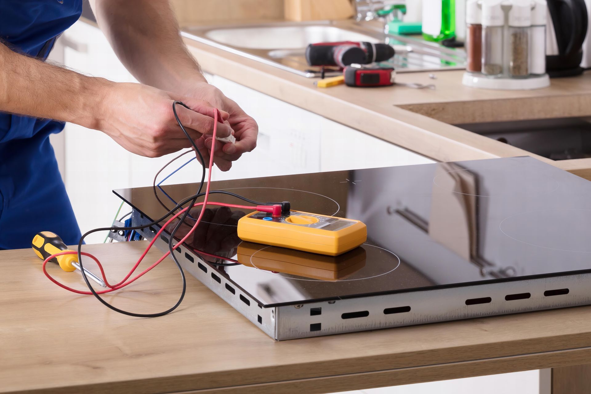 Technician repairing induction stove in kitchen.