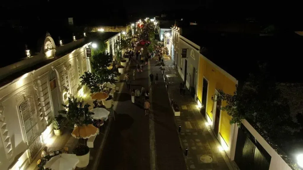 An aerial view of a city street at night with people walking down it.