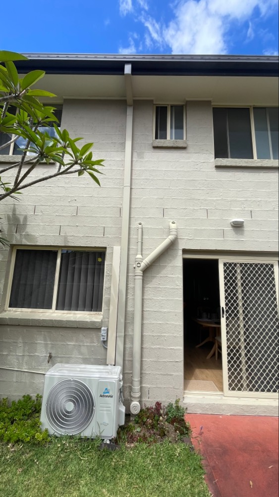 Exterior view of a two-story building with white brick walls, a sliding door, and an air conditioning unit.