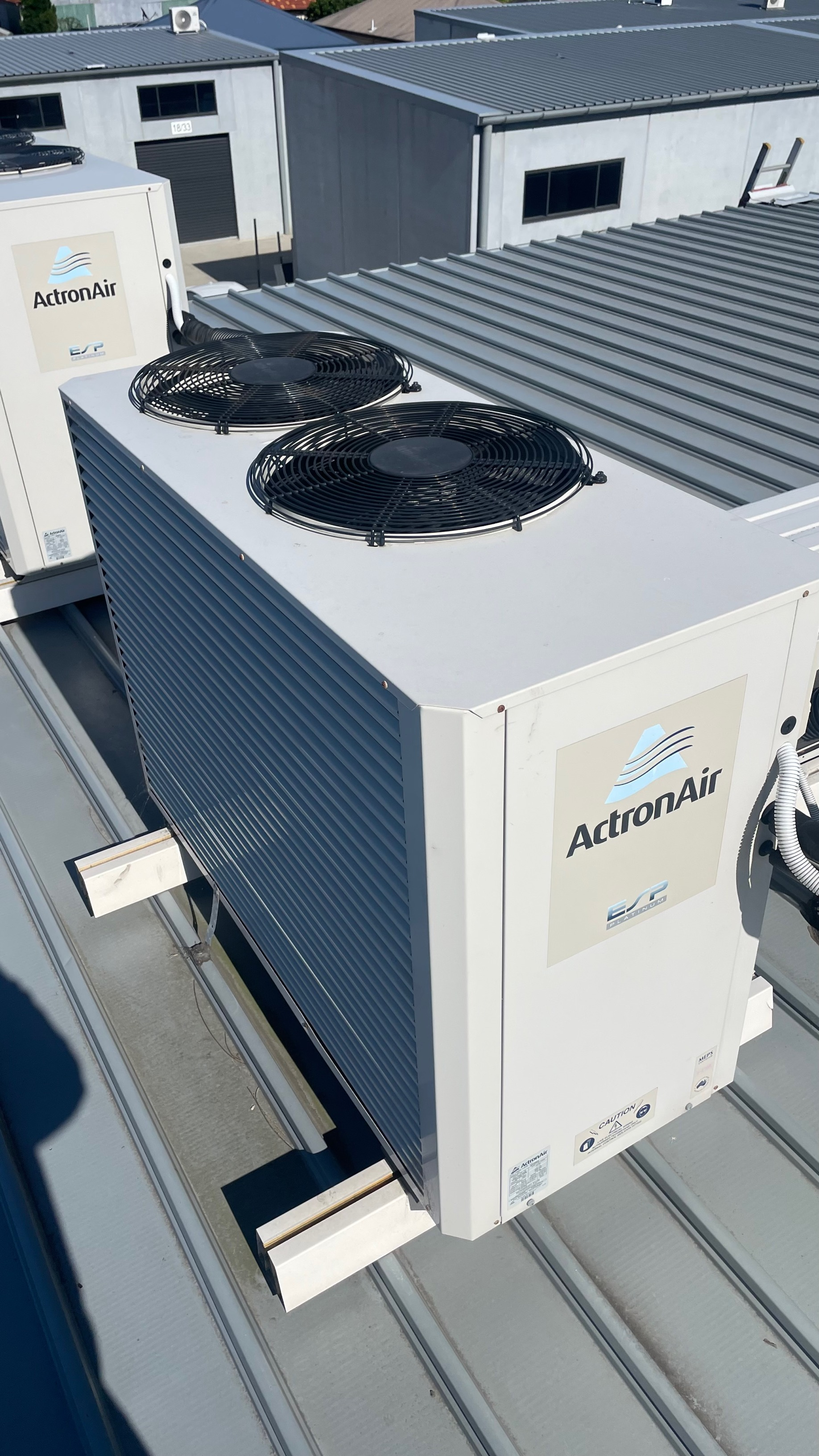 Two white industrial air conditioning units on a rooftop with fans on top and the word 