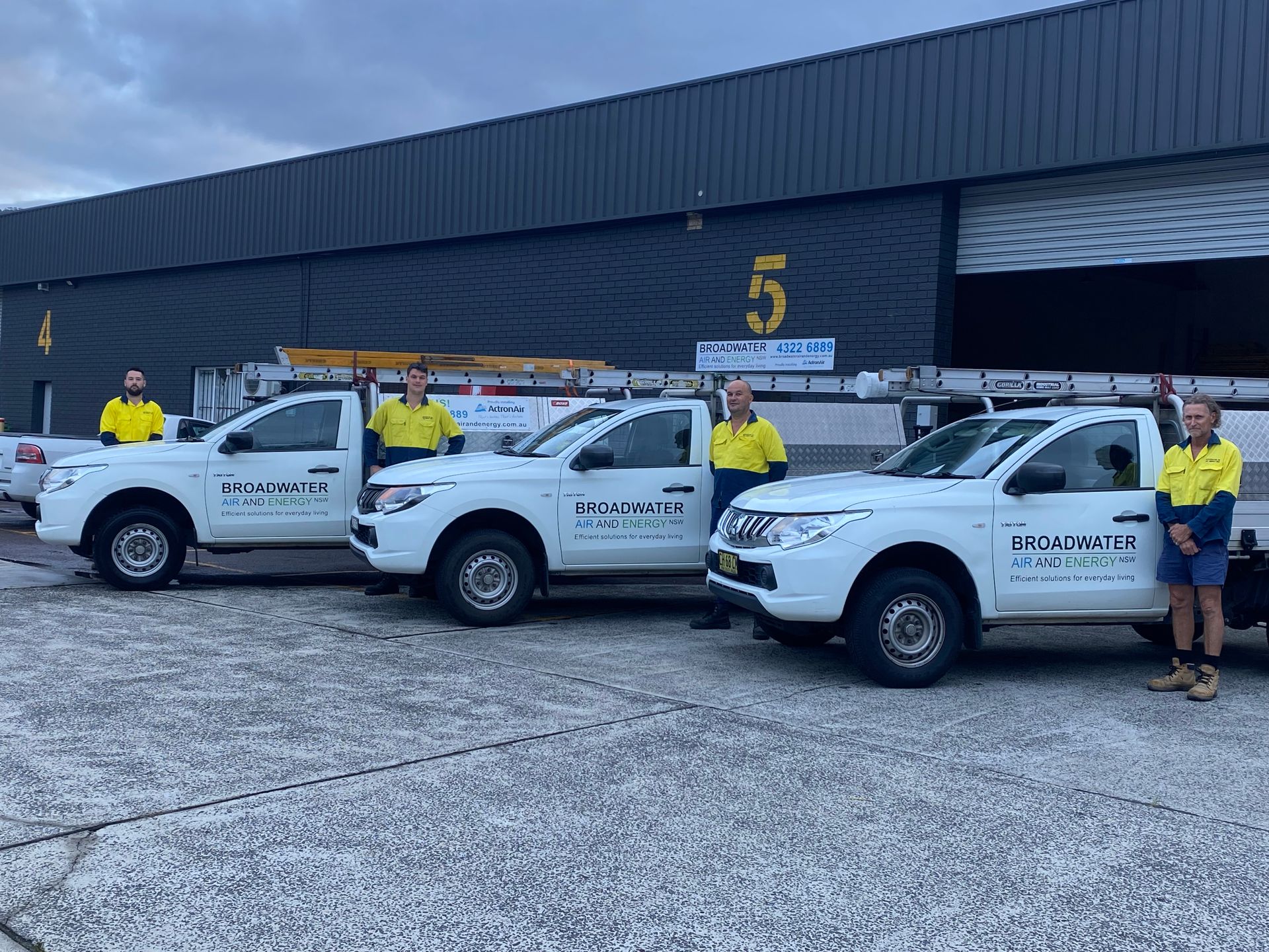 Three white work trucks with employees in front of a building.