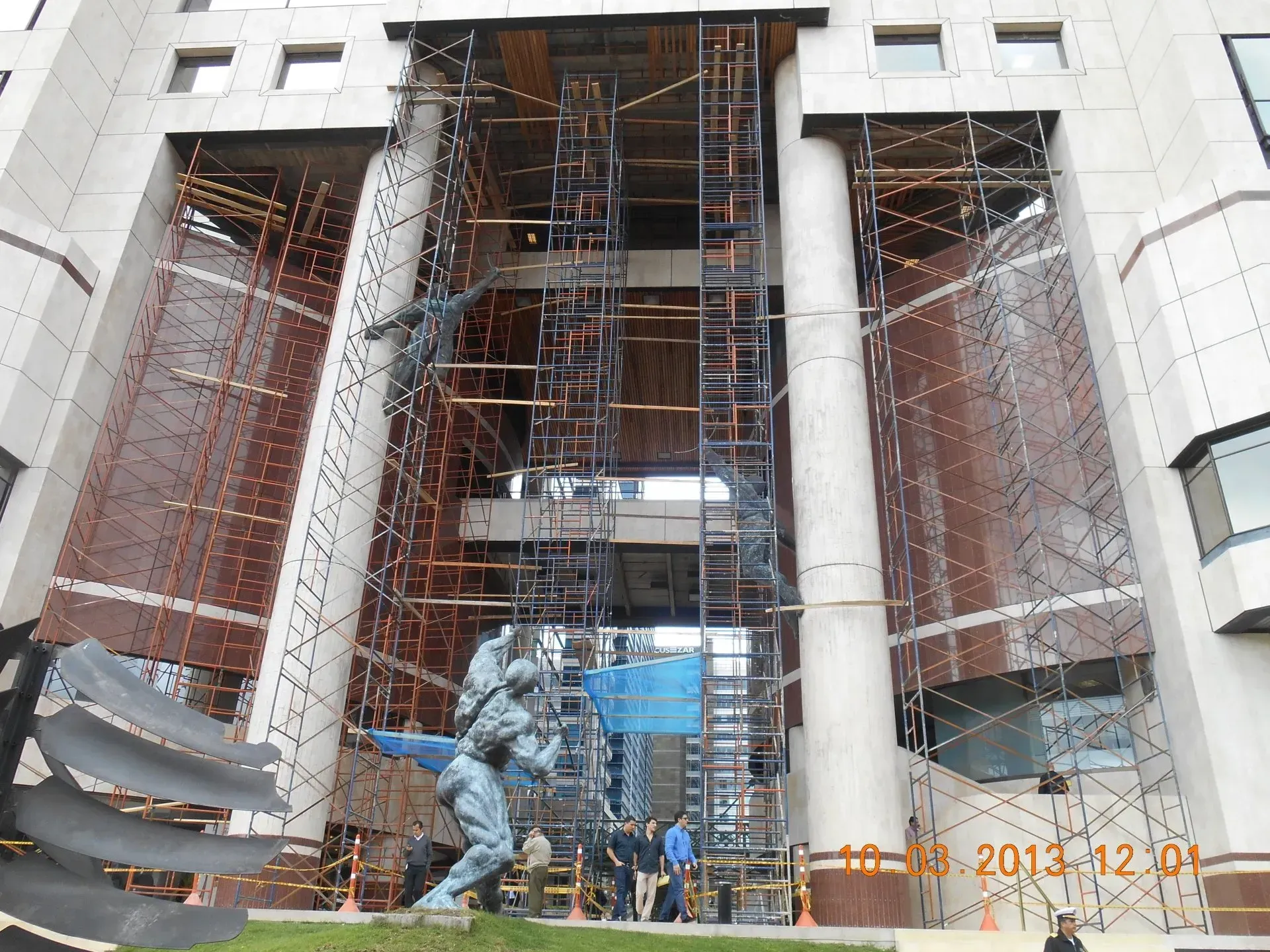 Obra en construcción con andamios y trabajadores en la entrada de un edificio grande