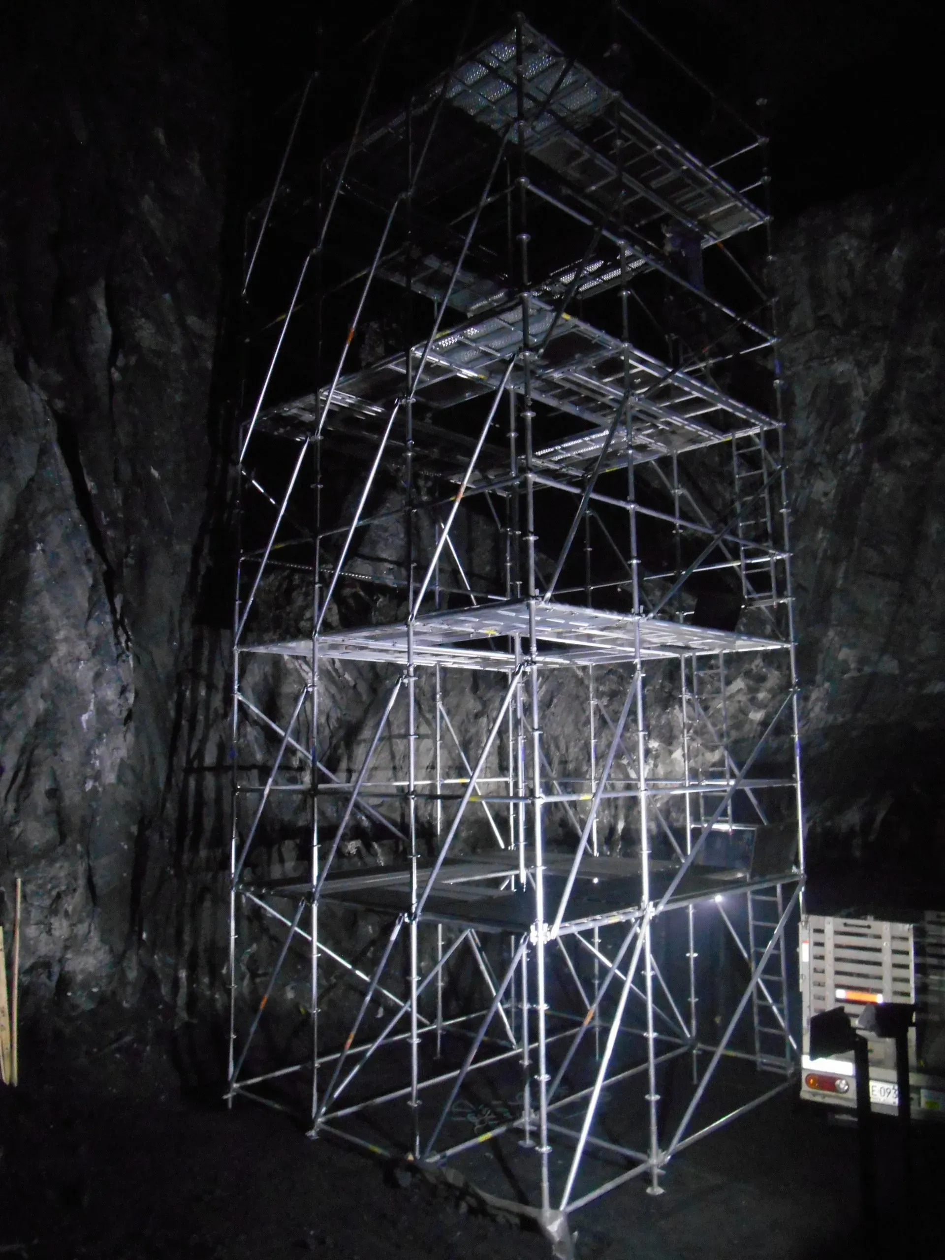 Torre de andamios en el interior de una caverna oscura, iluminada por potentes luces de trabajo.