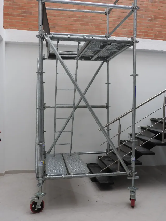 Edificio en construcción con andamios, cubierto con una lona protectora azul y una sección de la torre parcialmente terminada