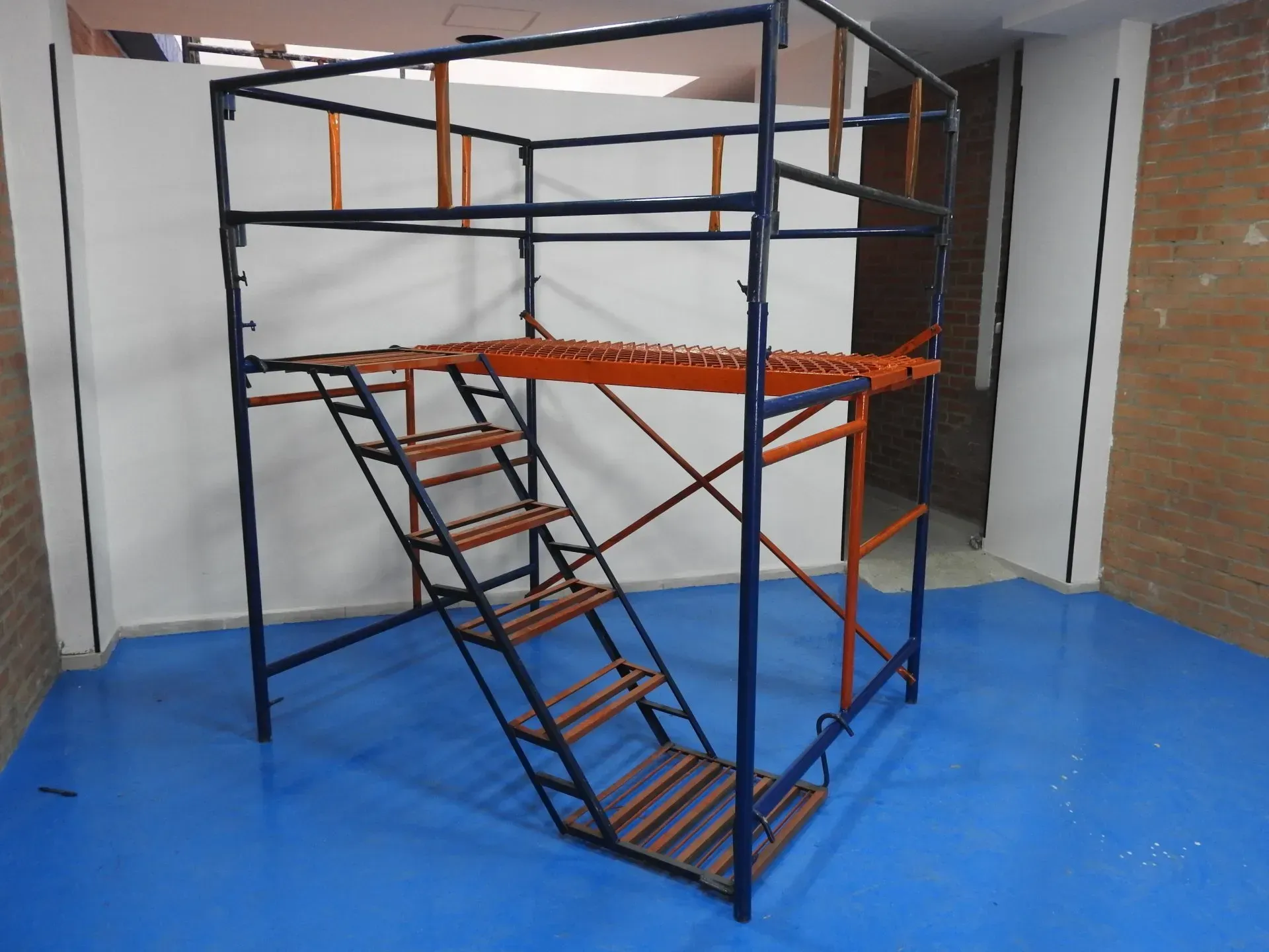 Andamio con estructura metálica, escaleras y plataforma en una sala con suelo azul