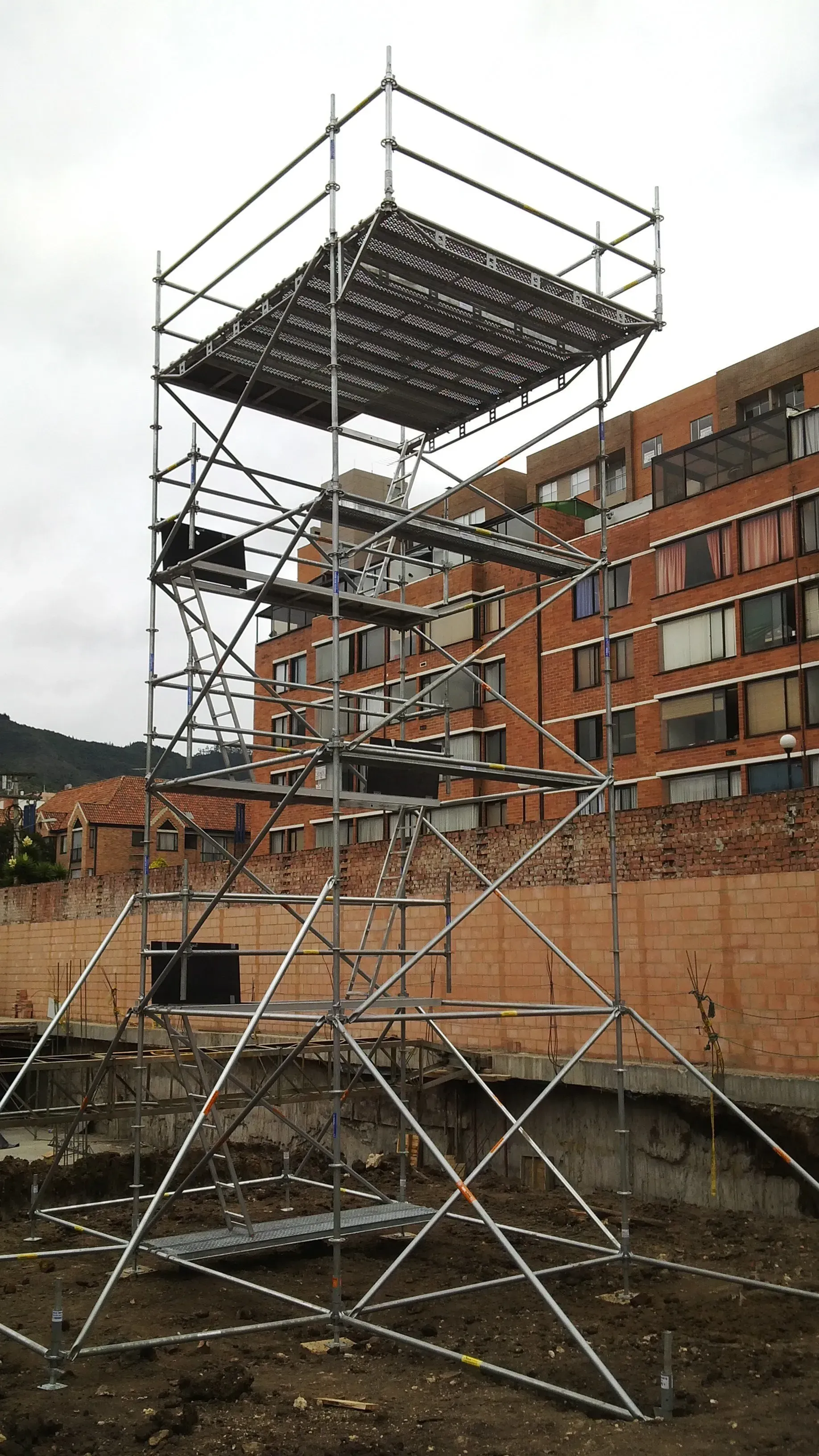 Torre de andamios junto a un edificio de apartamentos de ladrillo, con una plataforma en la parte superior en construcción.