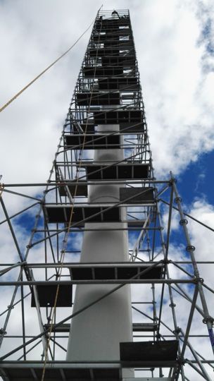 Andamios con una escalera amarilla junto a una estructura parcialmente construida bajo un cielo azul