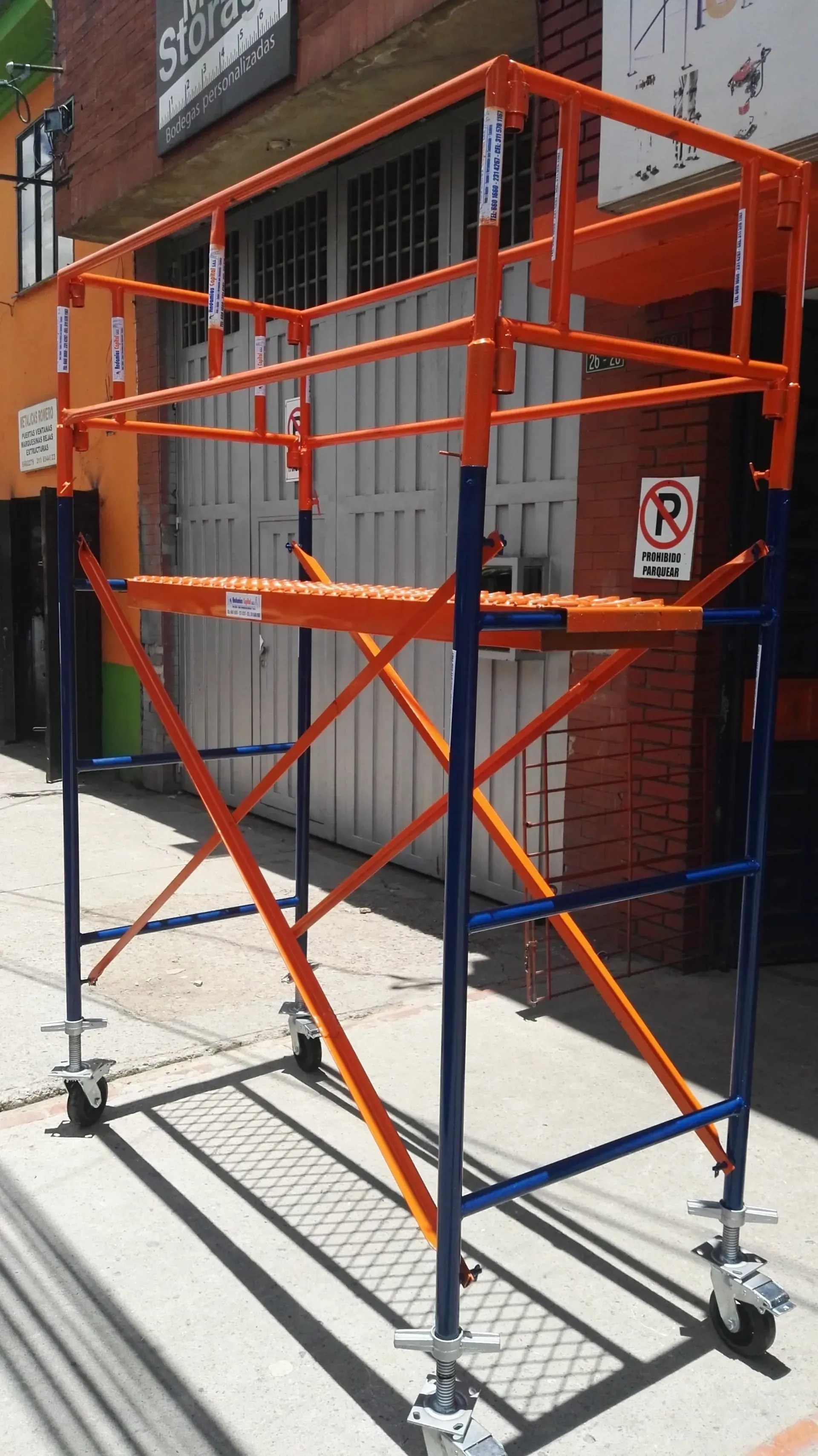 Andamio de obra naranja y azul en una acera junto a un edificio de ladrillo.