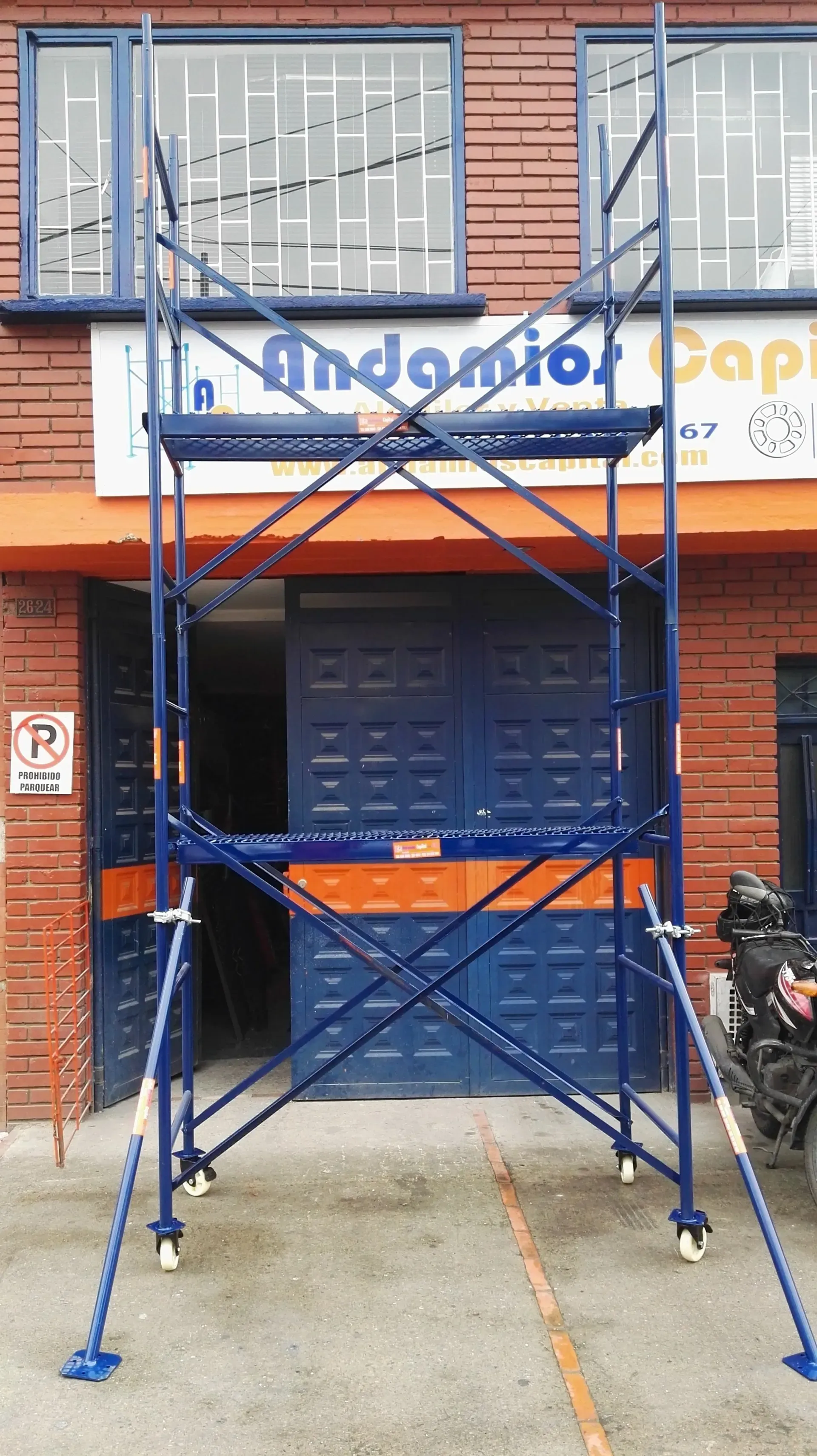 Un andamio metálico azul está montado frente a un edificio de ladrillo con un local cerrado con la persiana bajada.