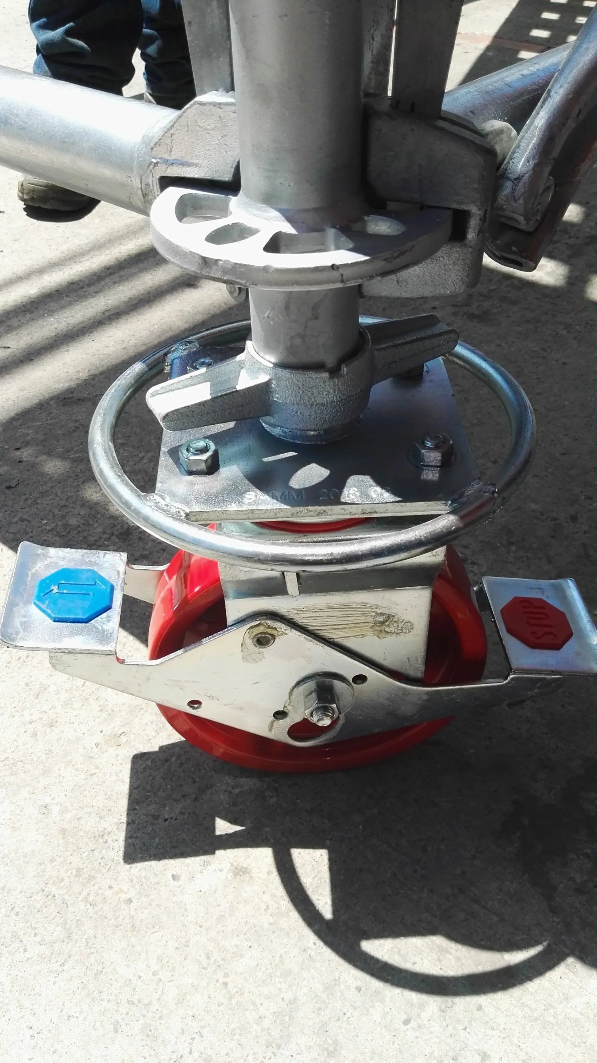 Primer plano de un dispositivo mecánico rojo y azul con abrazaderas y una base metálica circular montada sobre una superficie