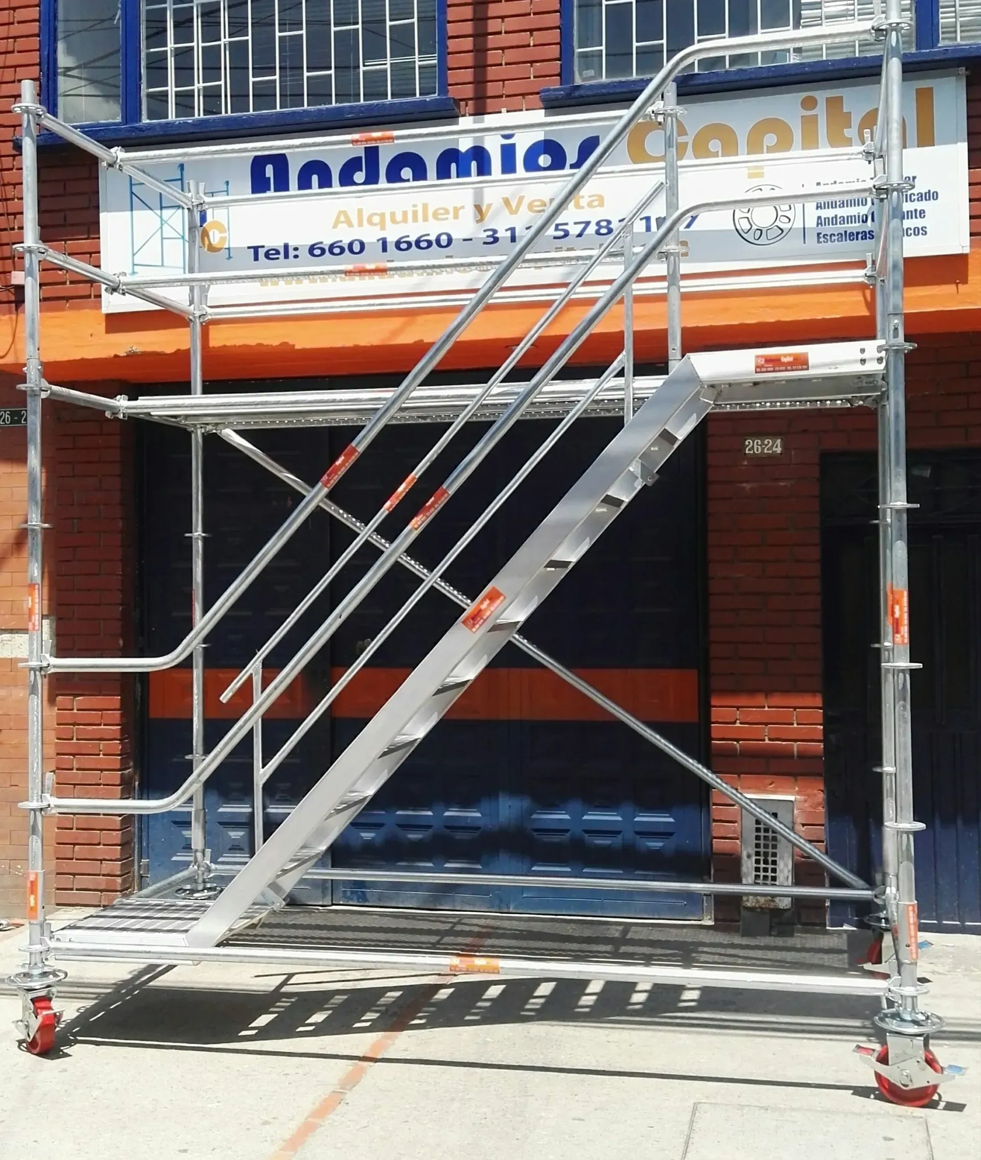 Andamio con escaleras metálicas frente a un edificio de ladrillo y el rótulo de un local comercial