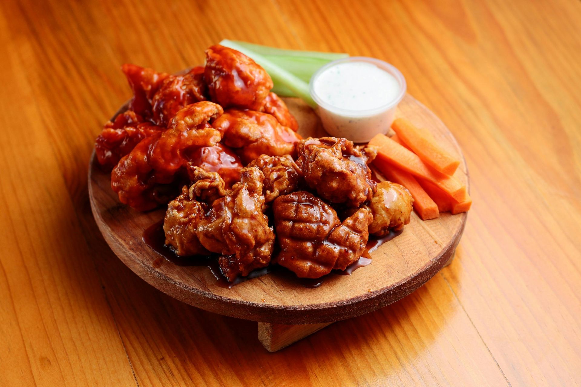 A wooden cutting board topped with chicken wings , carrots , celery and ranch dressing.