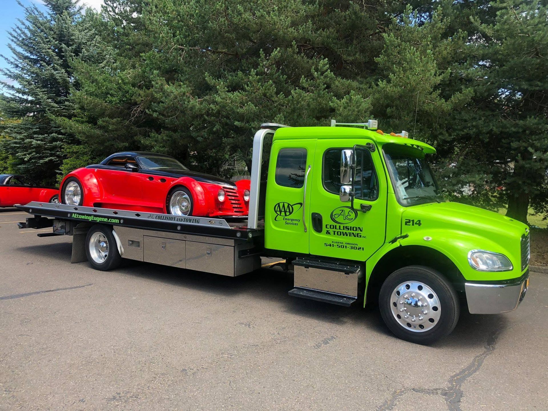 Bright green tow truck hauling a red sports car on a flatbed in a parking lot