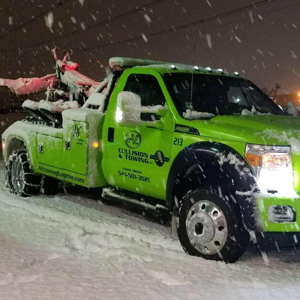 Bright green tow truck in heavy snowfall, carrying a snow-covered vehicle at night.