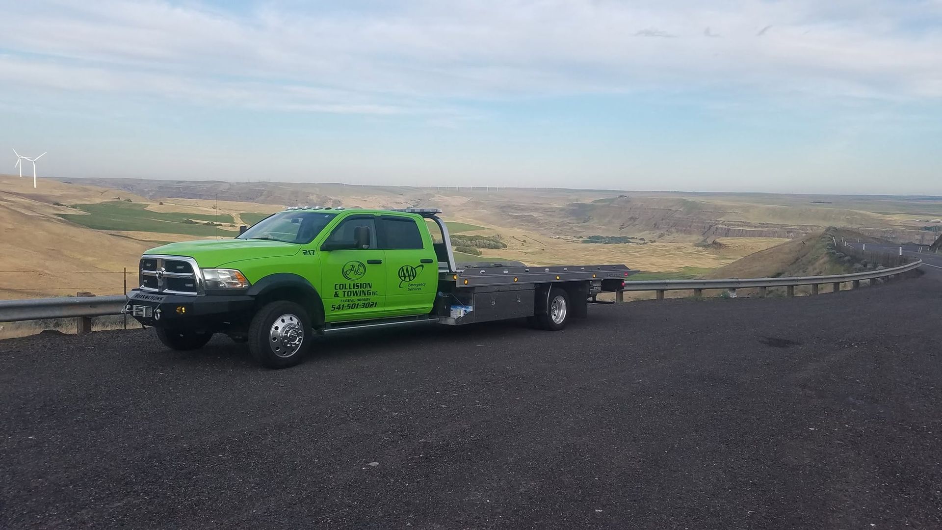 Bright green utility truck parked on a gravel road overlooking a desert valley