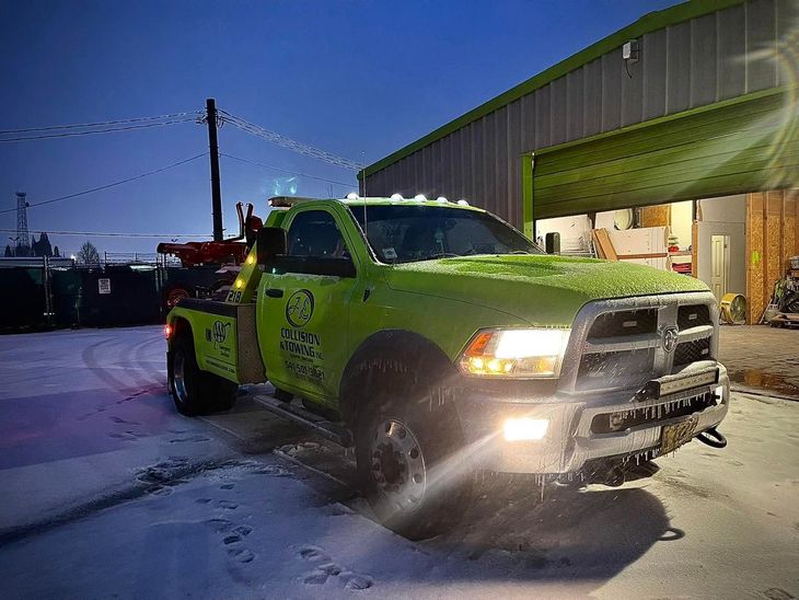 Bright lime-green pickup truck with snow on it, parked outside a lit garage at dusk.