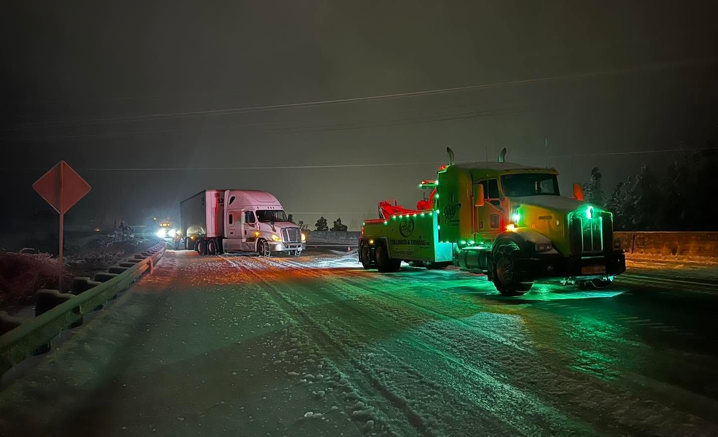Snowy road at night with a truck and heavy equipment lit in red and green lights
