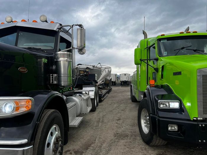 Two semi trucks parked side by side on a gravel lot under cloudy skies