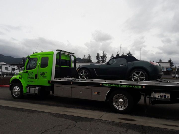 Bright green tow truck carrying a dark sports car on a flatbed under a cloudy sky